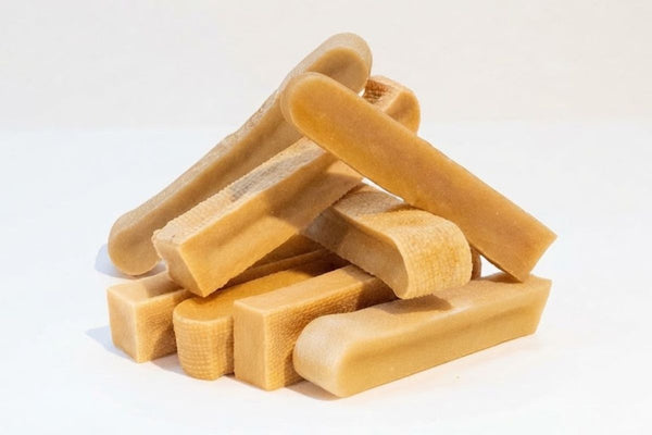 Several yak bar dog chews stacked on a white surface, showing their pale colour and texture