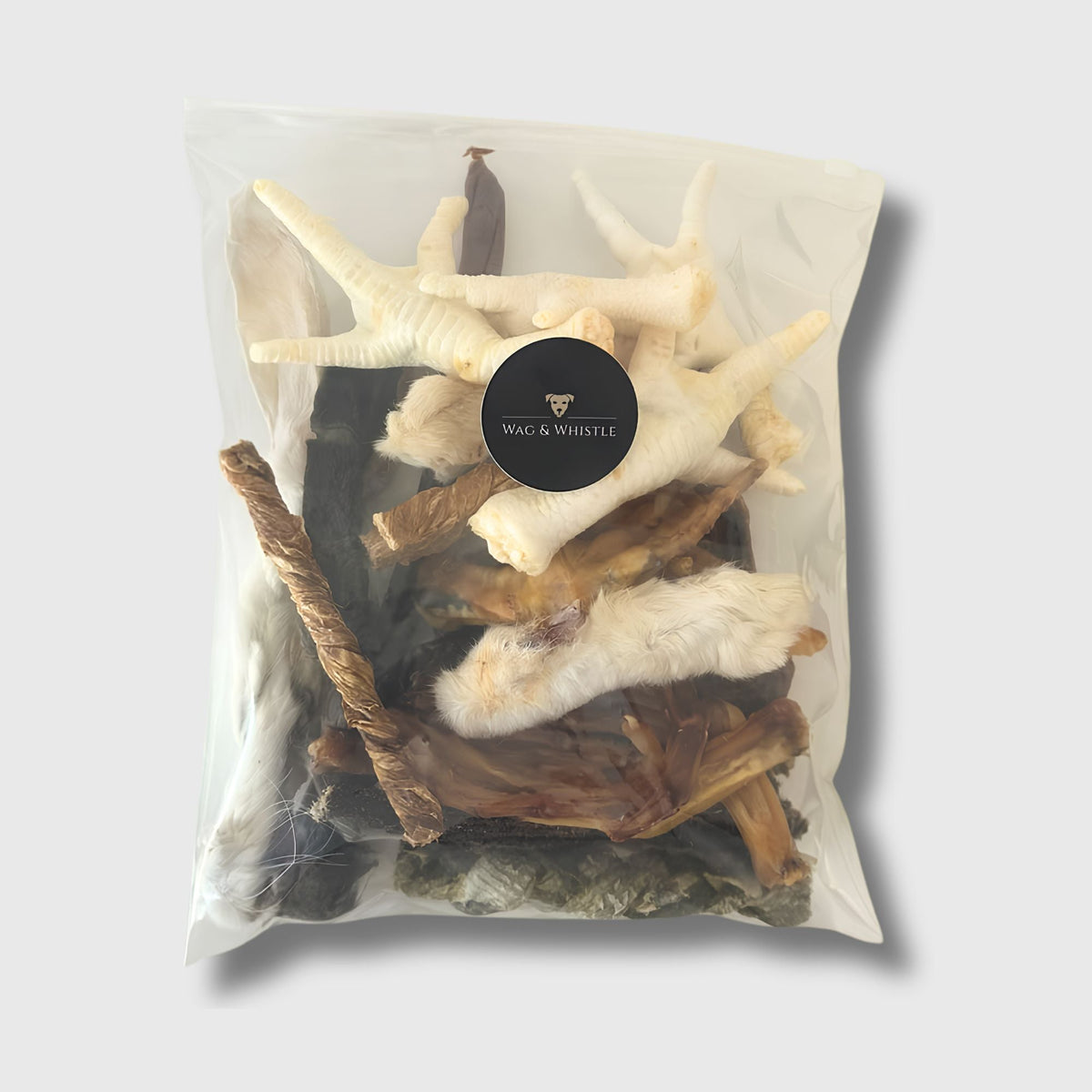 A sealed Wag & Whistle bag of mixed natural dog treats, with chicken feet, rabbit ears and tripe sticks visible through the front