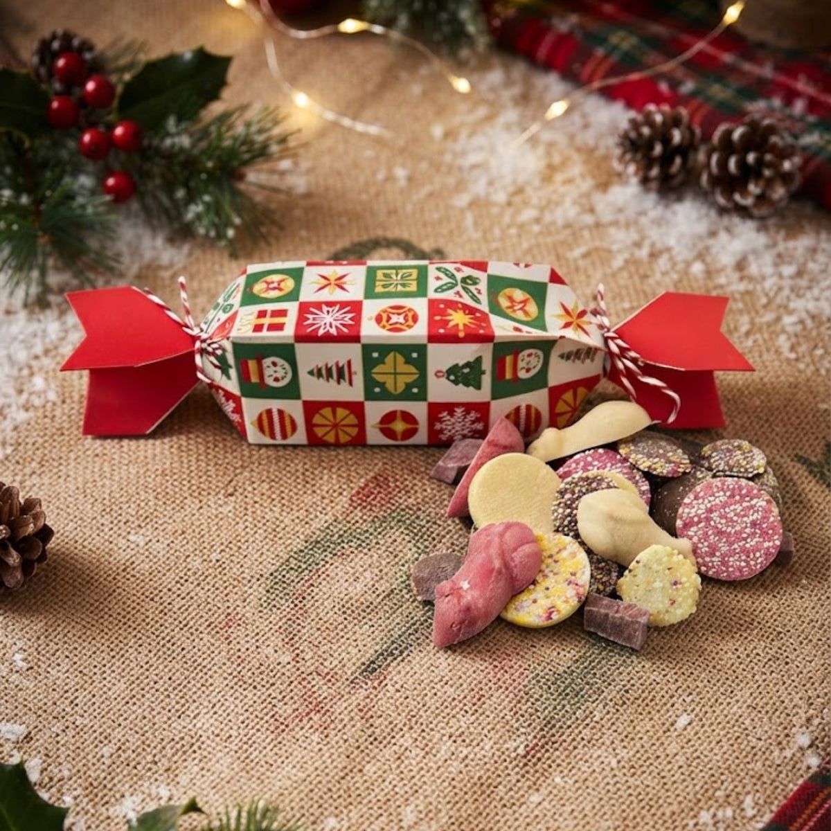 A Wag & Whistle dog Christmas cracker in red, green and cream, with a pile of pick n mix dog treats spilling out beside it