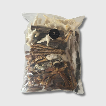 A large sealed Wag & Whistle bag packed with one hundred mixed natural dog treats, with chicken feet, rabbit ears and dried strips visible through the front